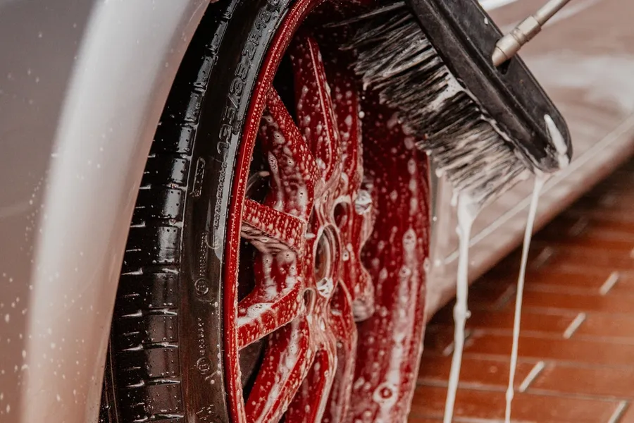 A soapy car wheel being cleaned with a detailing brush.