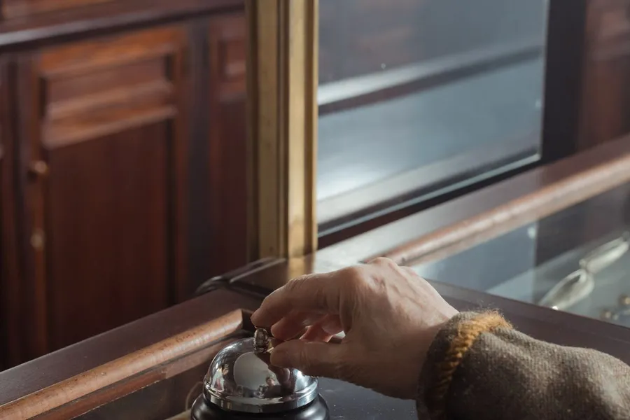 A hand ringing a service bell on a wooden shop counter.